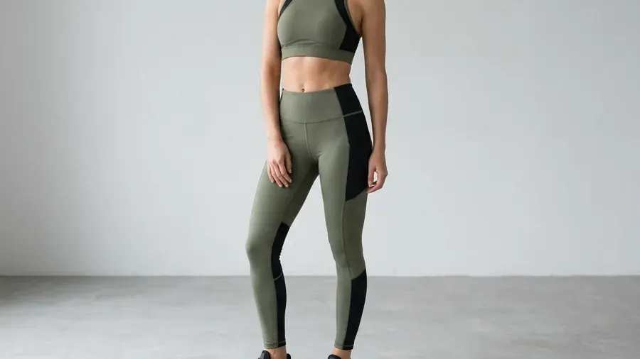 Woman standing in an olive green sports bra and olive and black color-block leggings