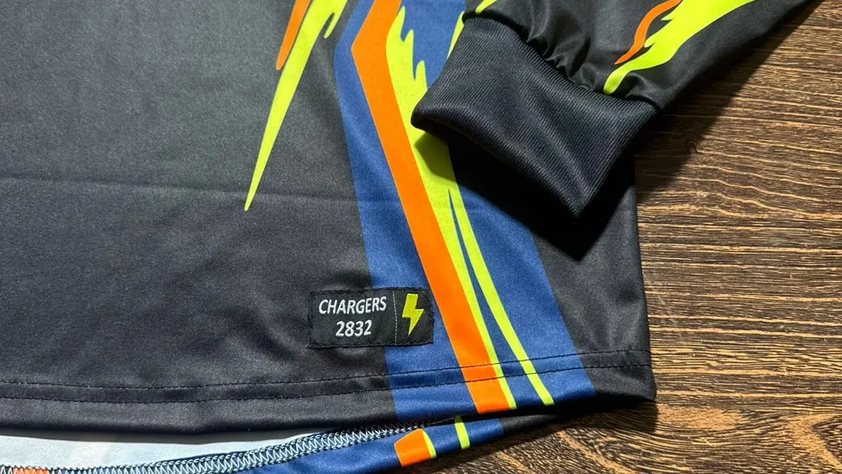 Close-up of the hem and cuff of a finished sublimated jersey, showing a woven label, printed stripes and overlocked stitching