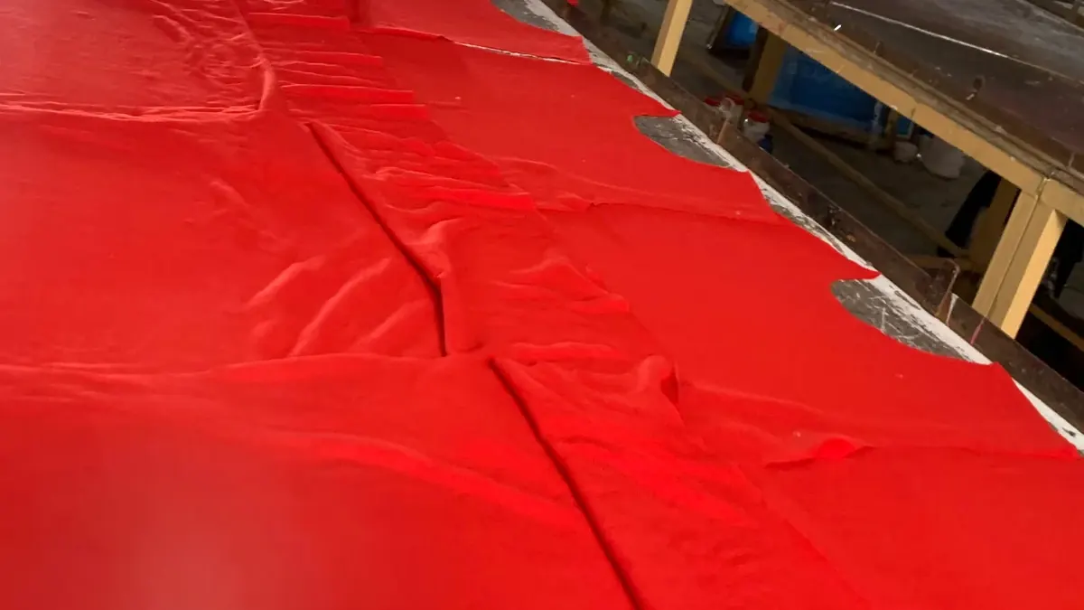 Red knit fabric laid out in layers on a long cutting table in the factory