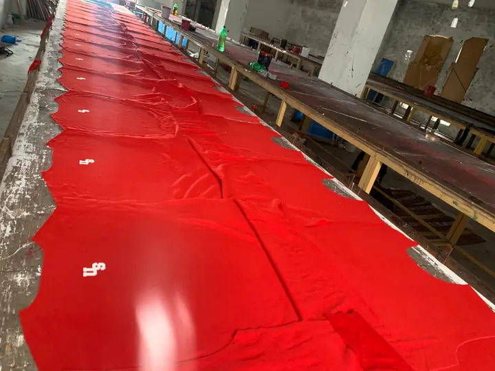 Long cutting table with red fabric laid out in layers ready for pattern cutting