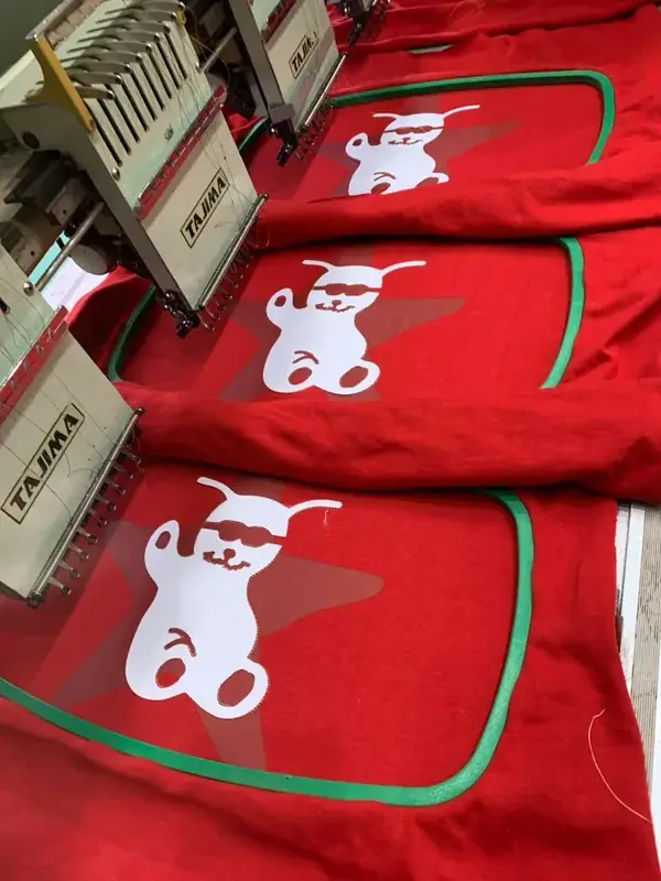 Close-up of an embroidery machine mid-stitch, mascot bear logo on red fabric