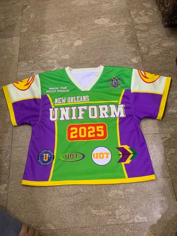 Custom sublimated lacrosse jersey, green purple and cream, "New Orleans Uniform 2025" team branding, front flat lay
